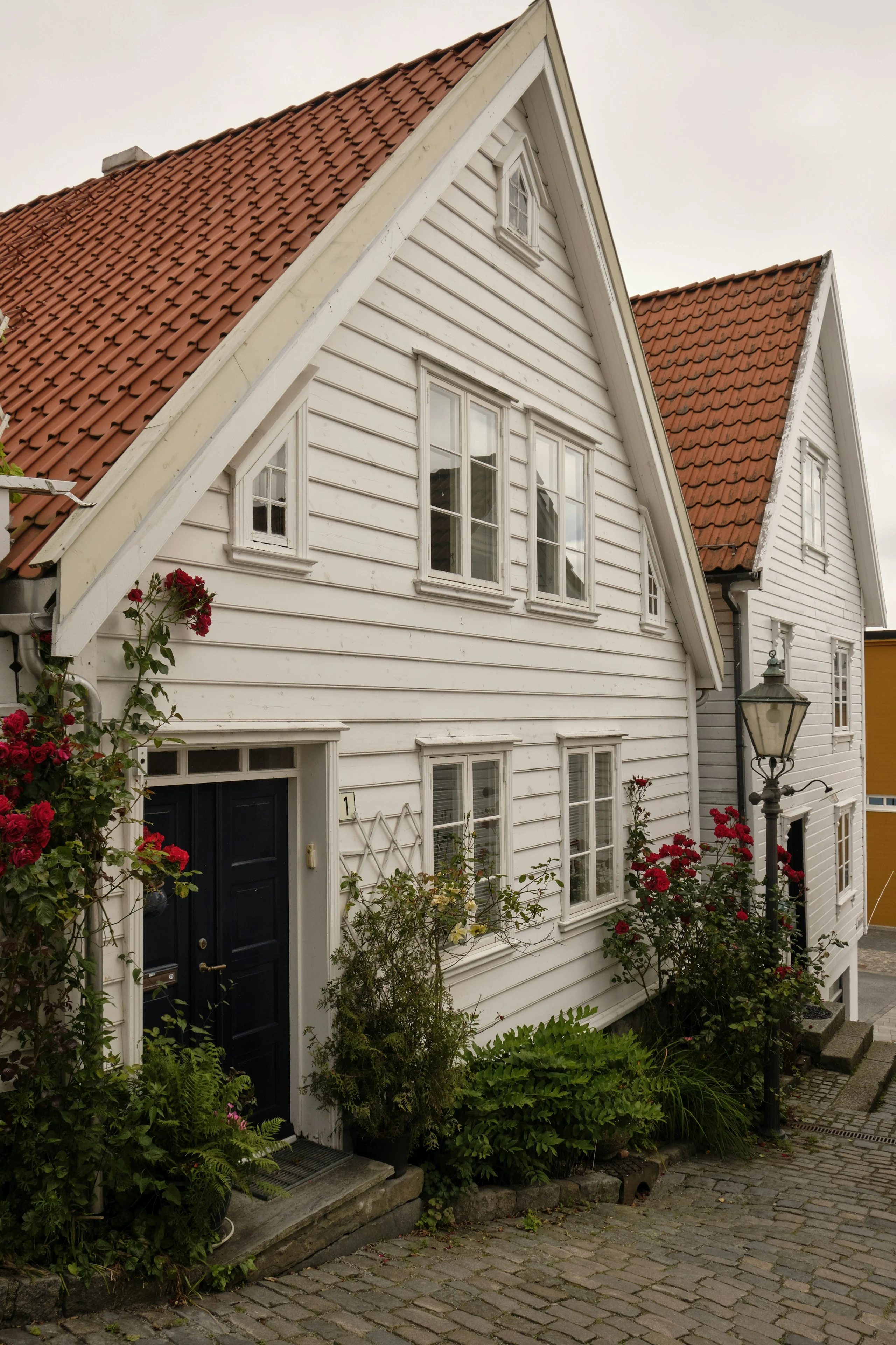 Hvit trehusfasade med rødt tak og blomster